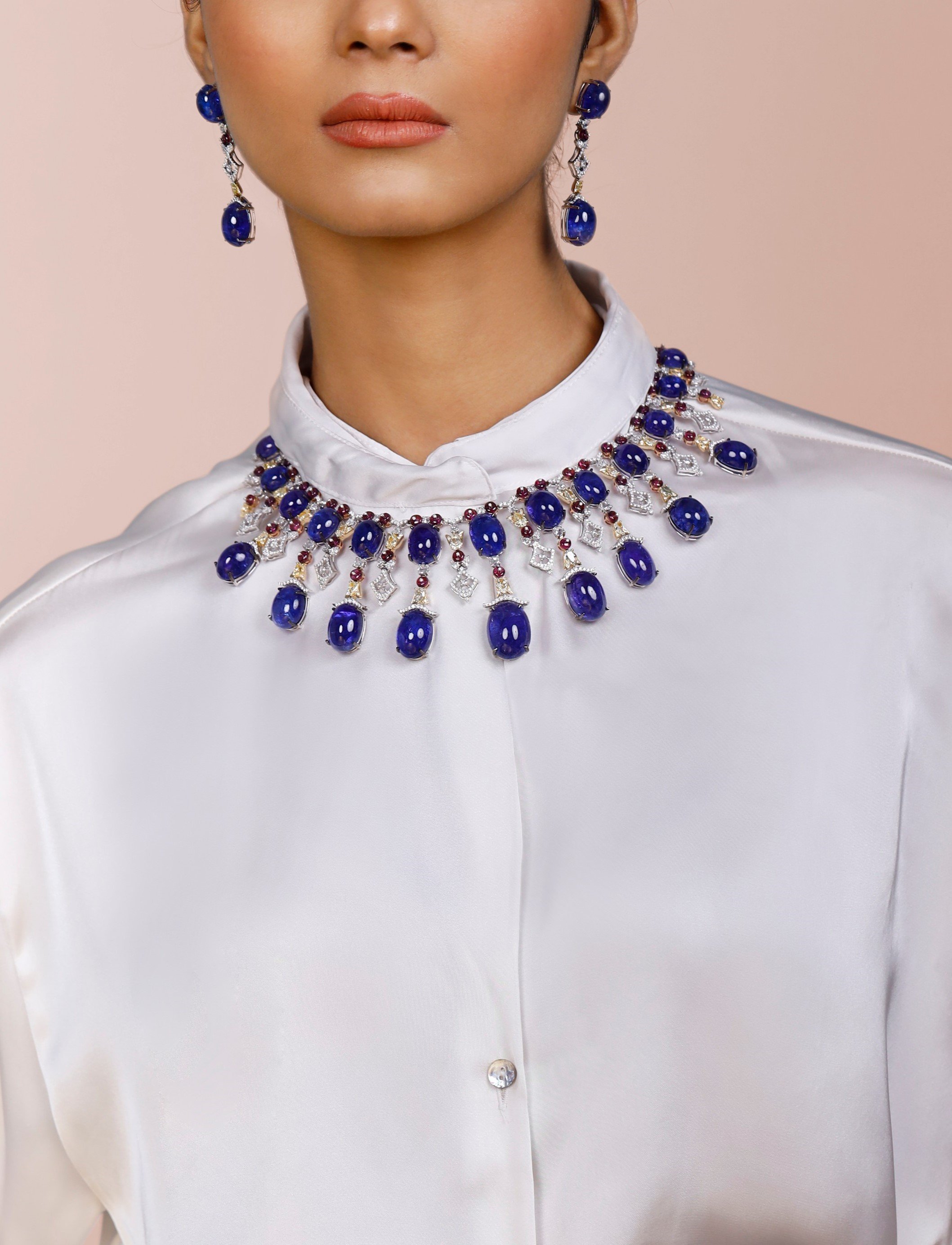 Un collar de cabujones de tanzanita, rubí y diamantes con aretes colgantes a juego, sobre una camisa de seda blanca